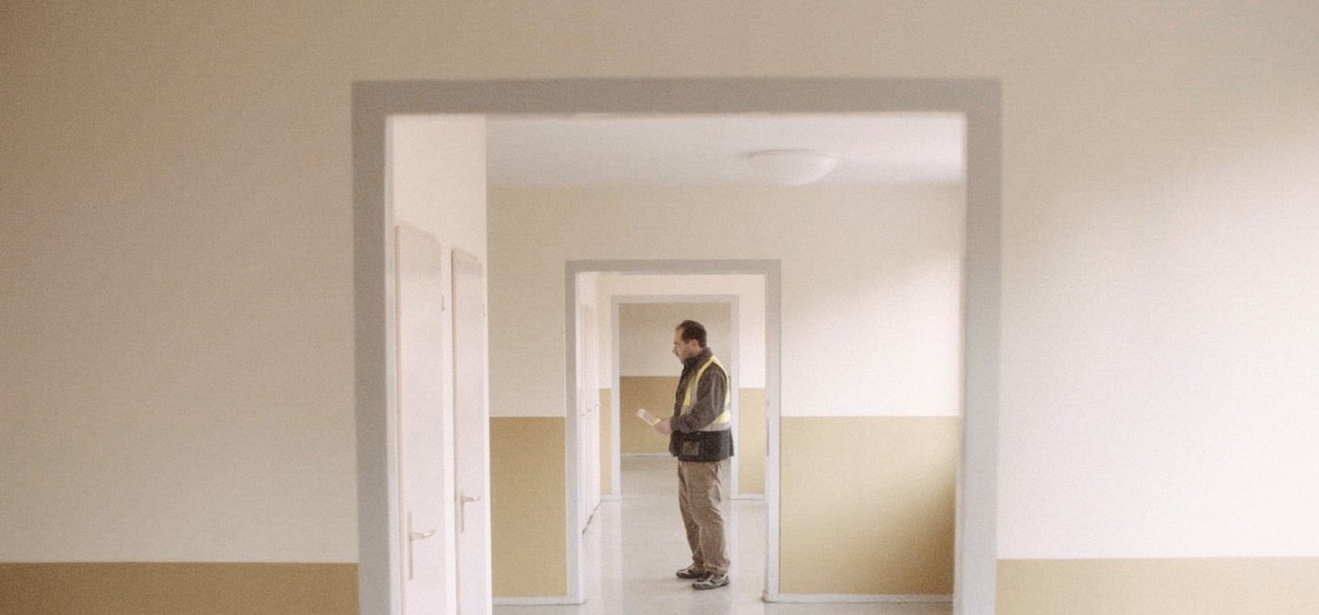 Eine in Hellbraun gekleidete Person steht in einem leeren Flur.