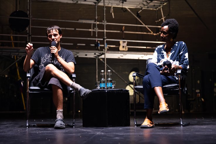 Nemó Flouret und Arlette-Louise Ndakoze stehen während Beyond the Stage auf der Bühne. Im Hintergrund des Bildes ist die Metallkonstruktion der Produktion zu sehen.