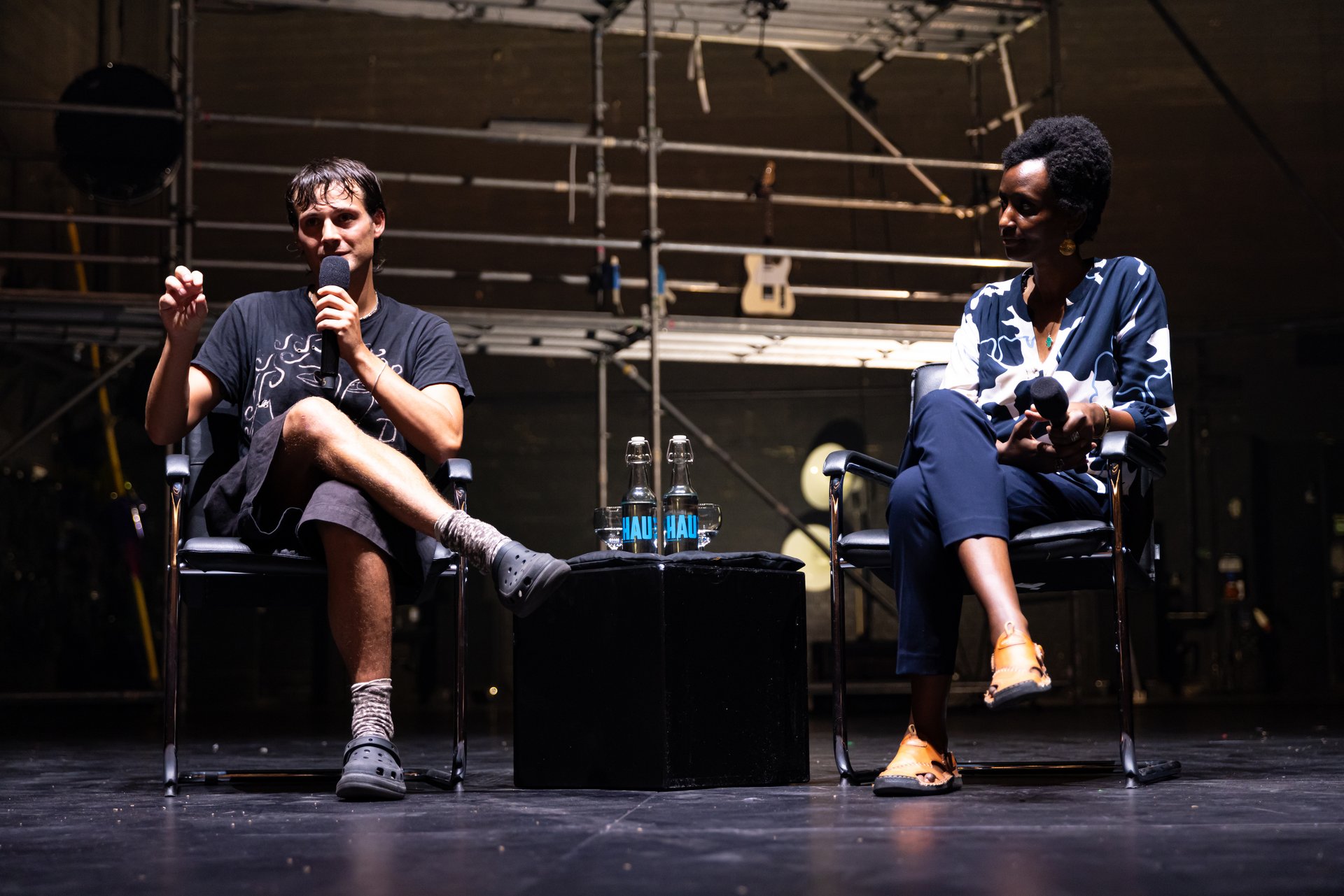 Nemó Flouret und Arlette-Louise Ndakoze stehen während Beyond the Stage auf der Bühne. Im Hintergrund des Bildes ist die Metallkonstruktion der Produktion zu sehen.