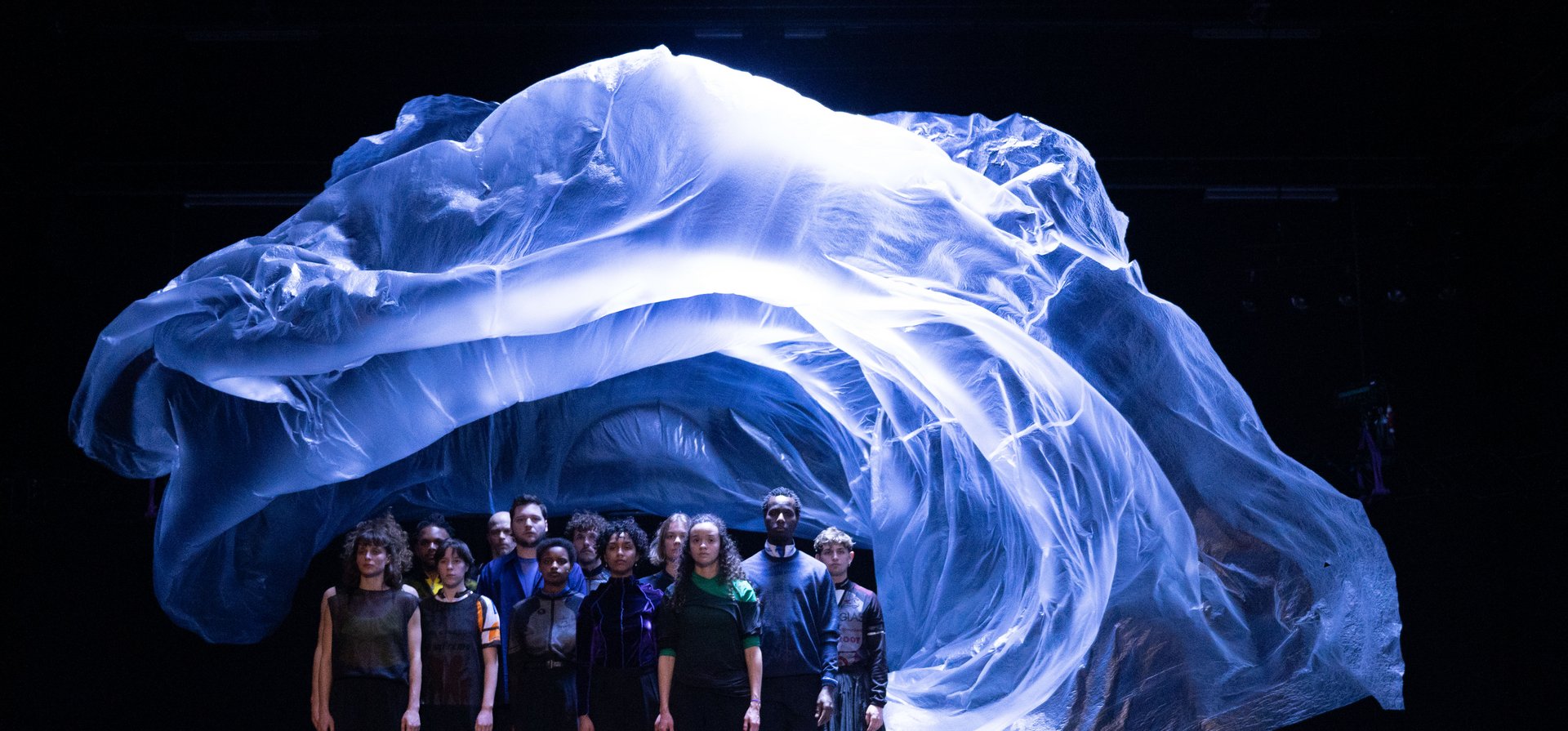 a group of dancers are standing in a black space under a bluely illuminated floating plastic that floats above their heads