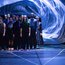 a group of dancers are standing in a black space under a bluely illuminated floating plastic that floats above their heads