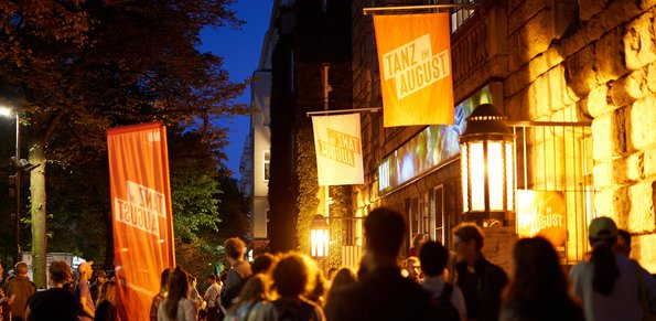 Auf dem Bild sind Menschen vor dem HAU1 nach der letzten Aufführung des Festivals zu sehen. Die Abendbeleuchtung ist eingeschaltet.