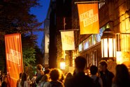 Auf dem Bild sind Menschen vor dem HAU1 nach der letzten Aufführung des Festivals zu sehen. Die Abendbeleuchtung ist eingeschaltet.