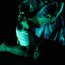 Zwei Performer:innen in intensiver Pose auf dunkler Bühne, grünlich beleuchtet, mit ineinander verschlungenen Körpern.