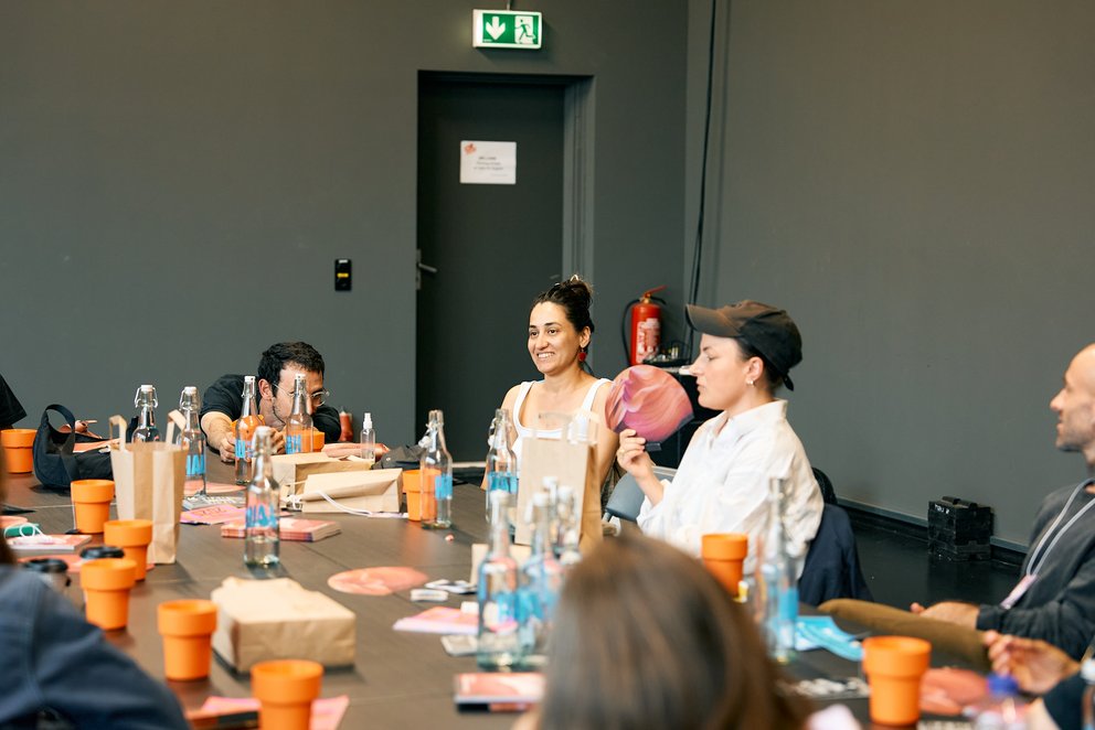 Auf dem Foto sieht man 5 Künstler*innen an einem Tisch, die sich unterhalten und kennenlernen. 