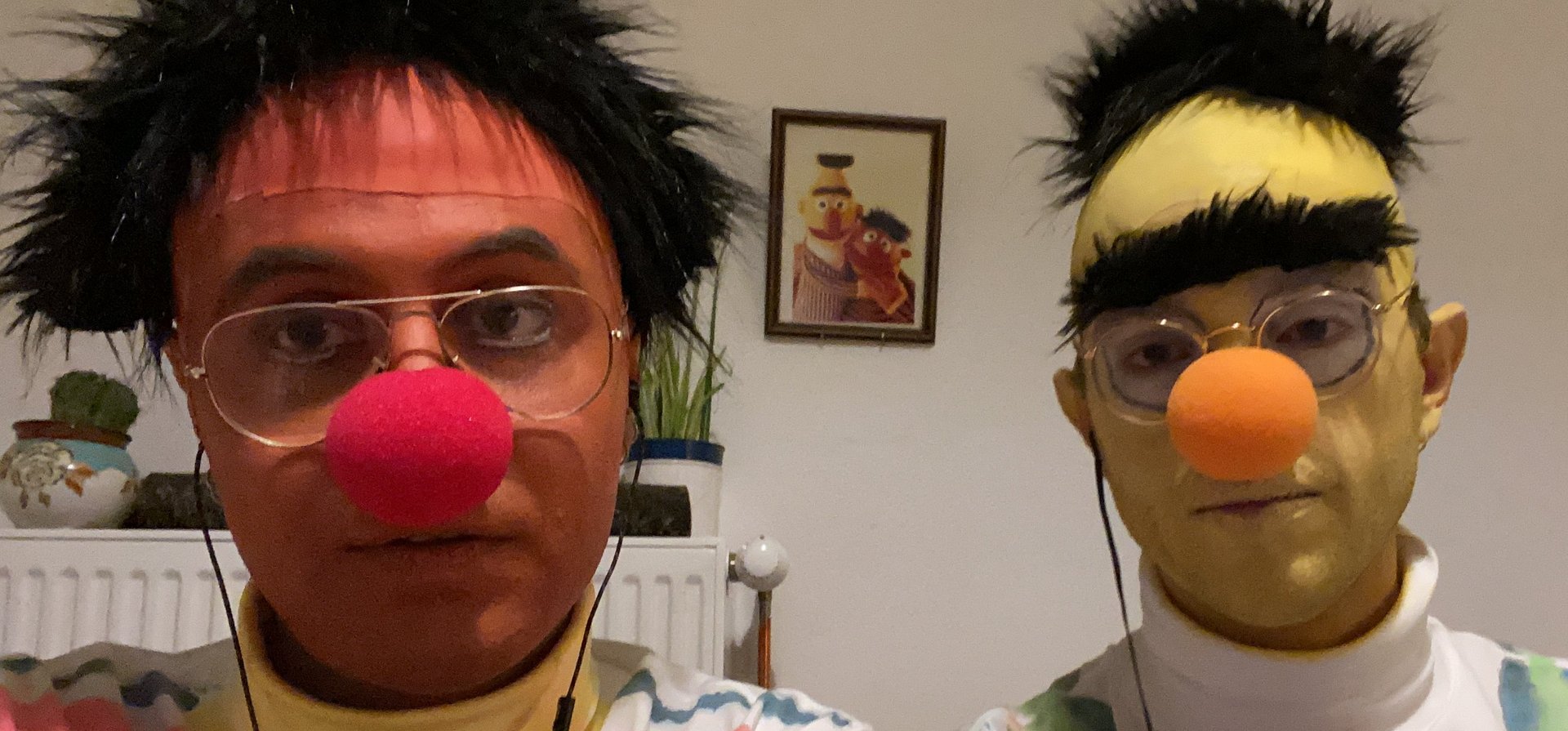 A selfie of two people costumed as Ernie and Bert from Sesame Street. In the background is a framed picture of the originals.
