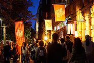 Auf dem Bild sind Menschen vor dem HAU1 nach der letzten Aufführung des Festivals zu sehen. Die Abendbeleuchtung ist eingeschaltet.