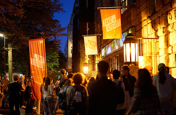 Auf dem Bild sind Menschen vor dem HAU1 nach der letzten Aufführung des Festivals zu sehen. Die Abendbeleuchtung ist eingeschaltet.