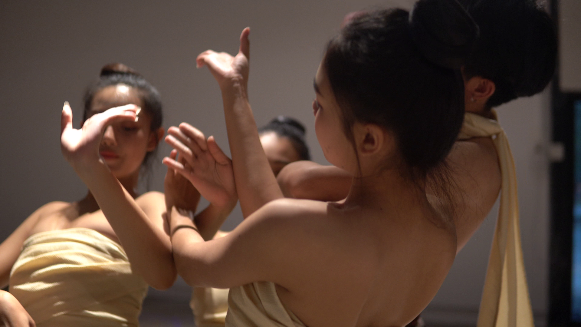Nahaufnahme mehrerer Performer:innen mit nacktem Rücken und beigefarbenem Stoff, die in konzentrierter Choreografie ihre Arme ineinander verschränken